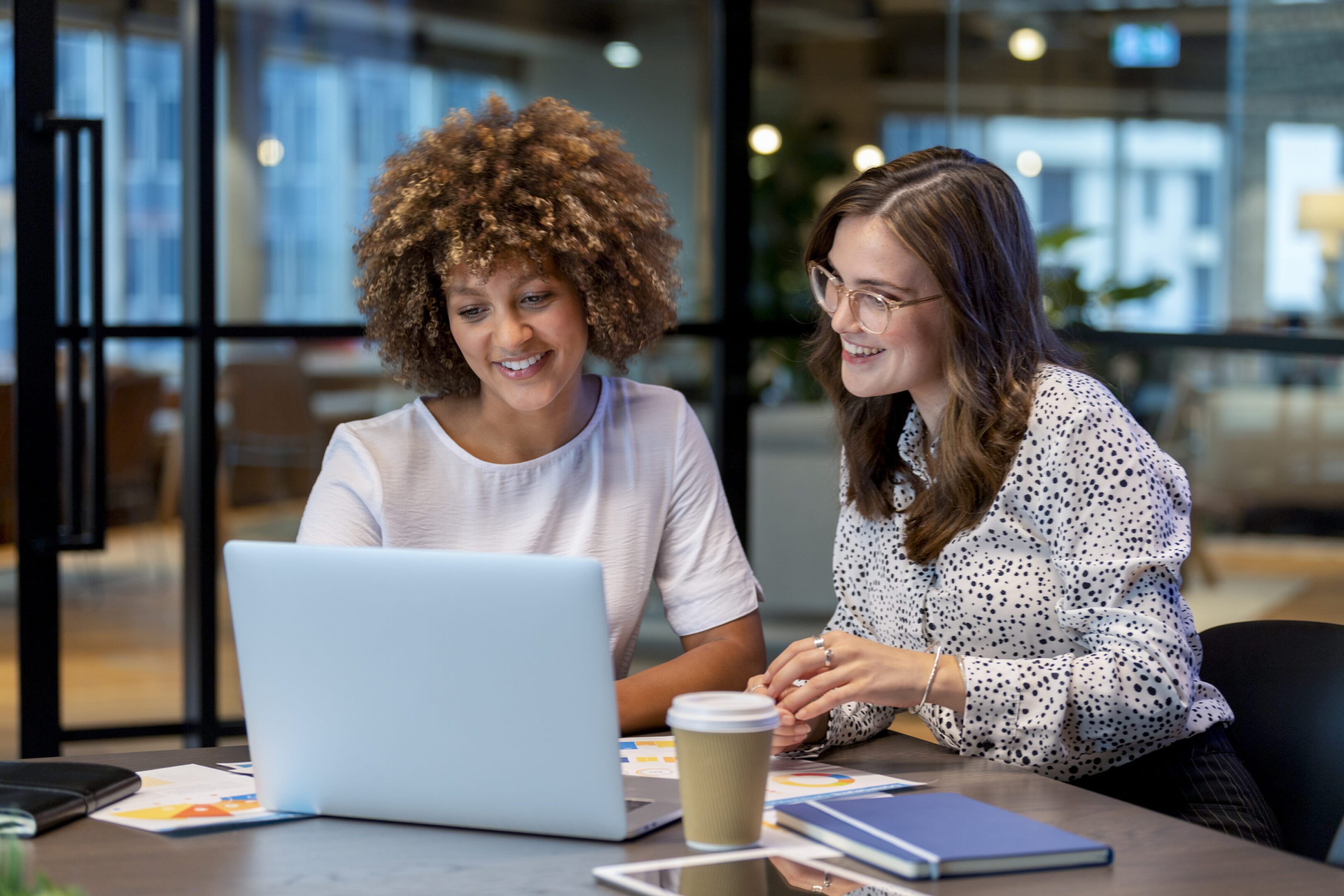 Two women working together on a laptop in a cozy cafe.